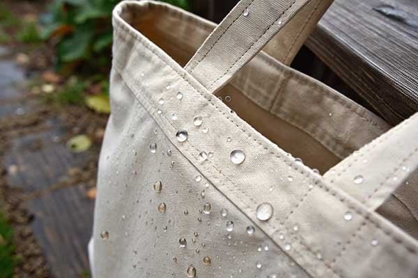 Raindrops cling to the surface of a canvas tote, hinting at its vulnerability to water.