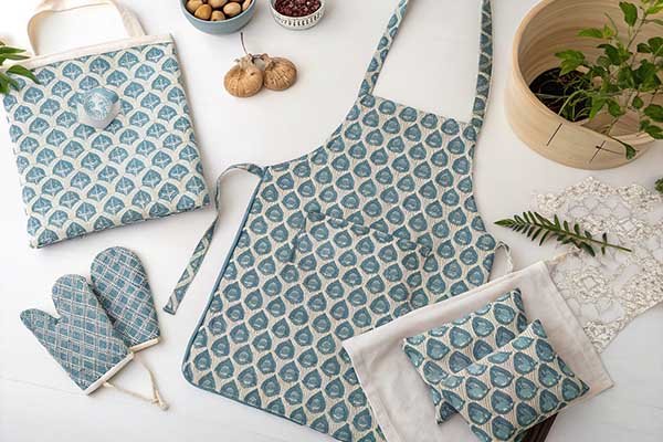 A flat-lay photograph showing an tote bag with a matching apron, cushion cover, and oven mitt artfully arranged around it.