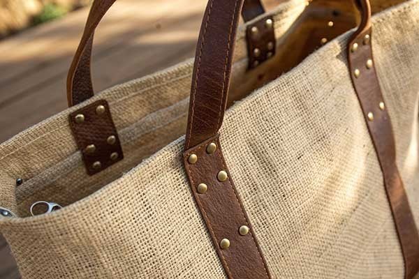 A close-up of a jute bag handle made from brown leather, with a metal rivet holding it to the bag