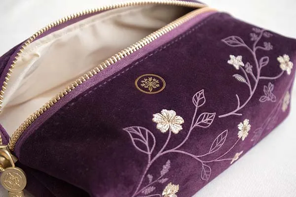 A purple pouch with floral embroidery, open to reveal a beige lining.
