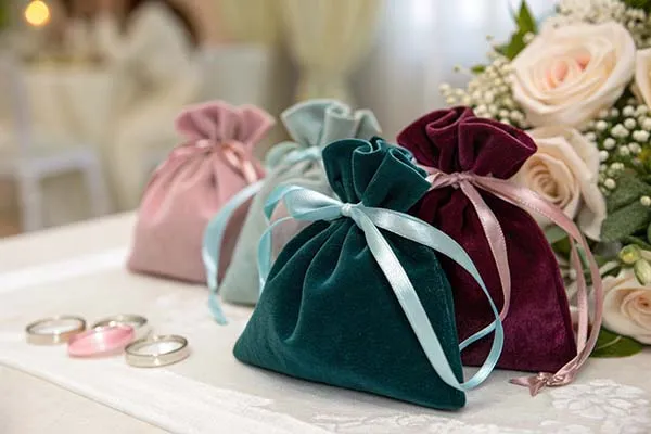 Three velvet bags in pink, teal, and burgundy with rings, ribbon, and flowers on a table.
