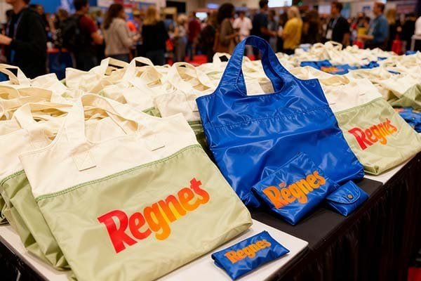 A spot at the exhibition site distributing foldable storage bags, with piles of beige and blue bags printed with logo.