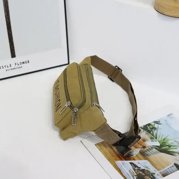 A khaki fashion waist bag with zippers placed on a white surface next to a picture frame and a magazine.
