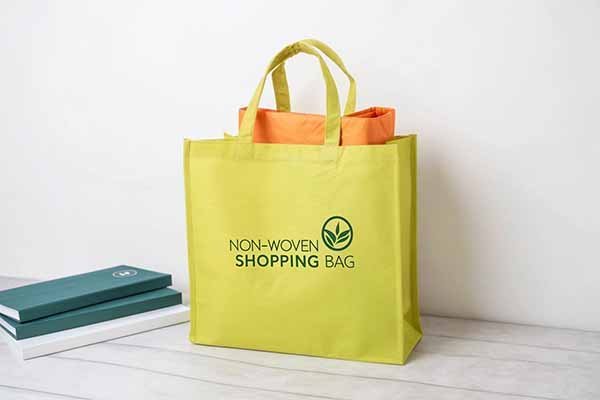 A bright yellow reusable shopping bag with a green logo printed on it.