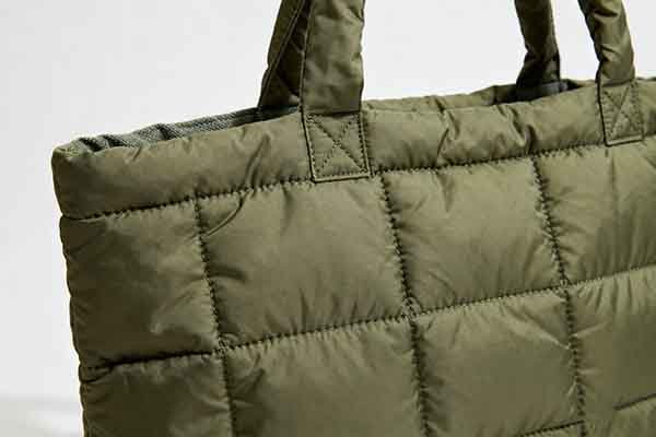 Close - up of an olive - green quilted puffy tote bag, showing the detailed quilted pattern.