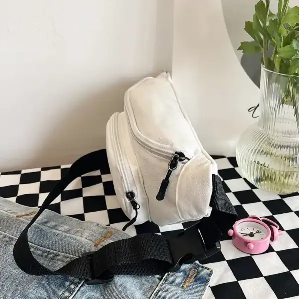 White canvas crossbody bag on a checkerboard surface with a pink clock and vase with green plant.