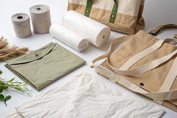RPET threads, Tyvek rolls, a khaki RPET tote bag, a green RPET top, and white fabric, accompanied by green plants, showcasing diverse applications of RPET and Tyvek in eco-friendly textiles