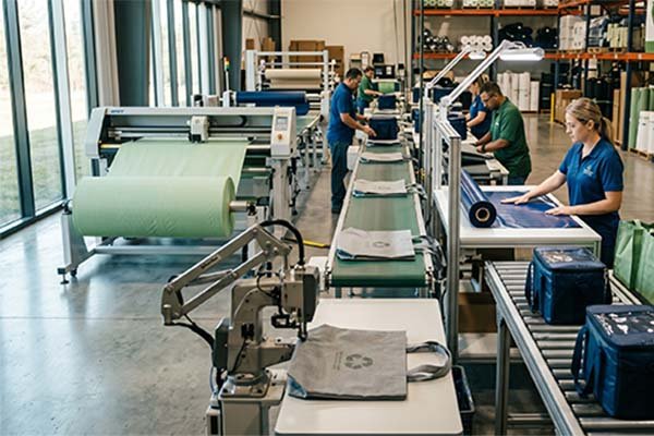 Factory workers operating machinery to assemble bags on a production line, highlighting actual manufacturing amid packaging cost instability.