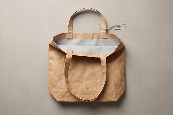 Top-down view of an open, brown double-layer Tyvek tote bag revealing a smooth grey inner lining, demonstrating a premium, structured design with a recycled material tag.