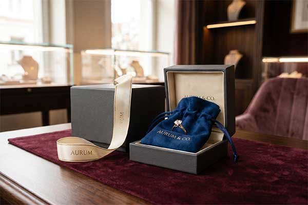 Layered jewelry packaging showing a ring inside an Aurum branded velvet pouch nestled within a rigid presentation box