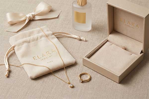 A custom branded Elara Jewelry velvet bag and matching open ring box displayed with gold jewelry