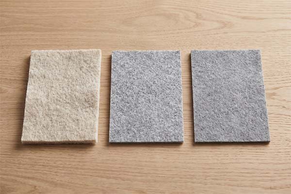 Three rectangular felt material swatches in beige, light grey, and dark grey laid flat on a wooden surface.