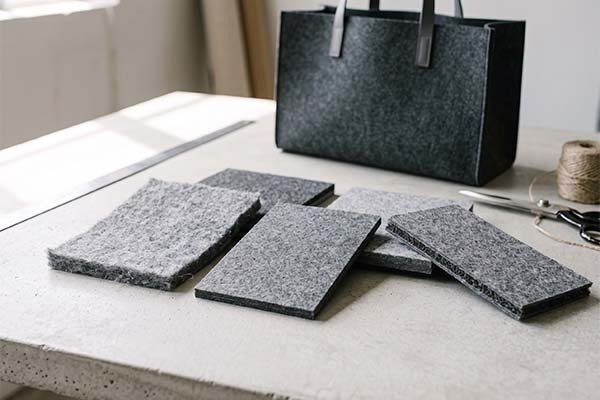 Comparing grey felt samples of different density and thickness on a table with a finished felt bag.