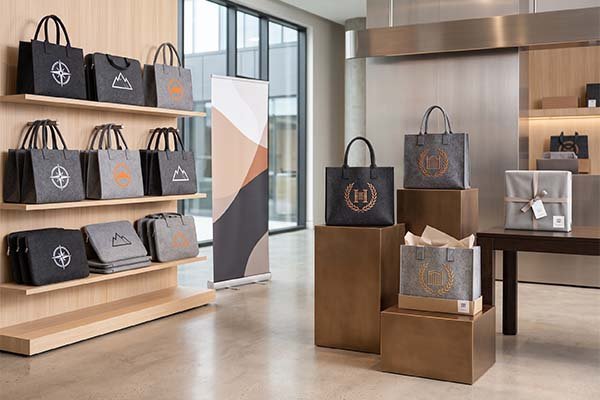 A modern showroom display featuring premium corporate gift and promo bags made of felt, highlighting branded totes, laptop sleeves, and boxed gift sets organized for different industries.