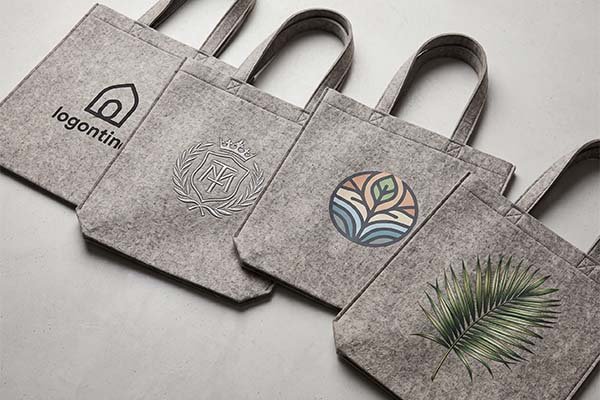 Four custom felt bags laid-side-by-side demonstrating various printing techniques on felt material, including minimal line art, detailed embroidery, and vibrant full-color graphics.