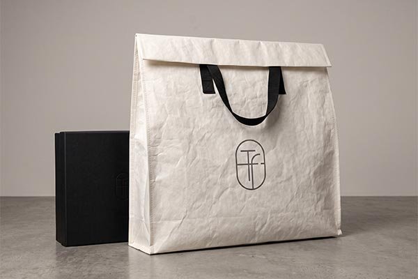 A premium white Tyvek shopping bag with black handles and a custom logo, placed next to a high-end matte black gift box, creating a luxurious unboxing experience.
