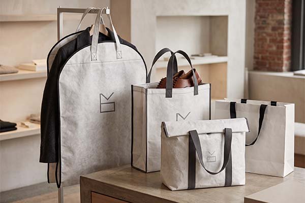 Tyvek packaging applications in a retail boutique setting, featuring a premium suit garment cover hanging on a rack and a tote shopping bag containing leather shoes.