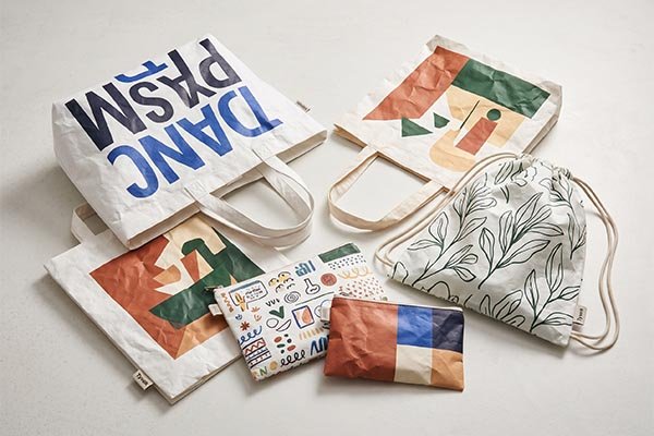 A flat lay display of printed Tyvek merchandise, featuring vibrant, abstract artistic designs on tote bags, a drawstring bag, and zipper pouches.