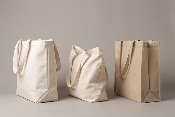 Three custom tote bags made from different textiles displayed side-by-side to compare fabric stiffness and bag structure.