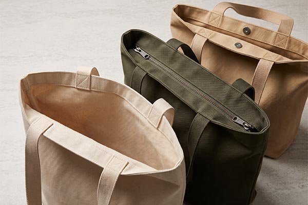 Close-up top view comparing zipper, magnetic snap, and open-top closure options for canvas tote bags.